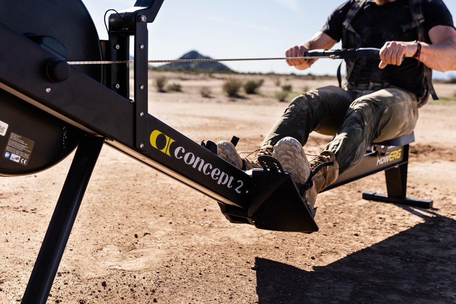 Person using a Concept2 rowing machine in an outdoor setting with mountains in the background