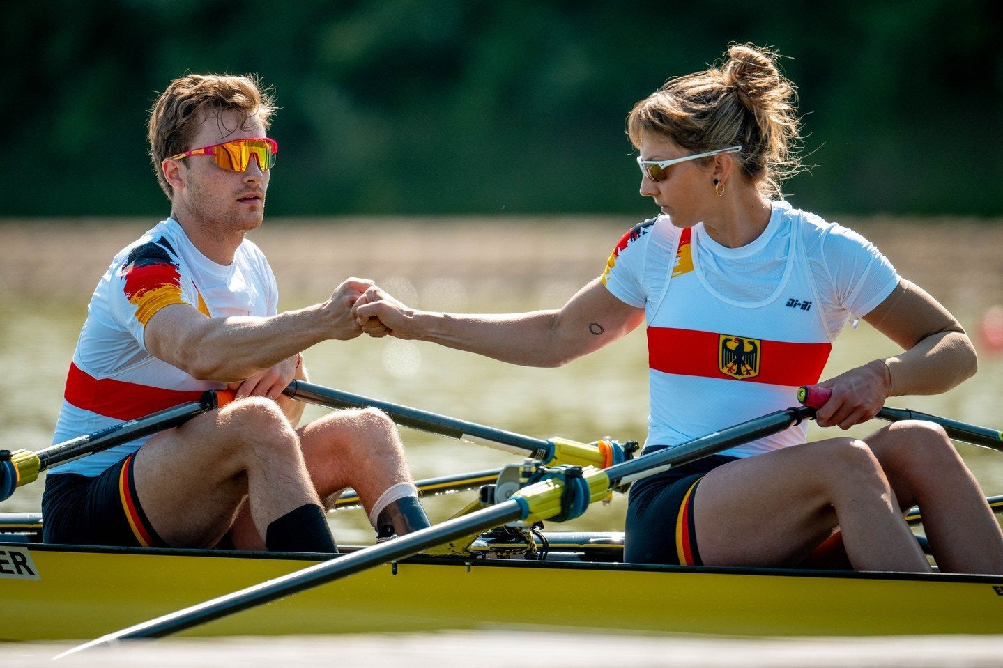 Two rowers from Germany shaking hands on a riverbank.