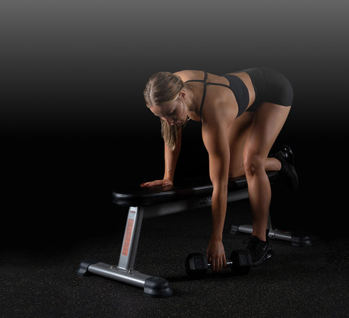Woman exercising with dumbbells on a weight bench against a dark background