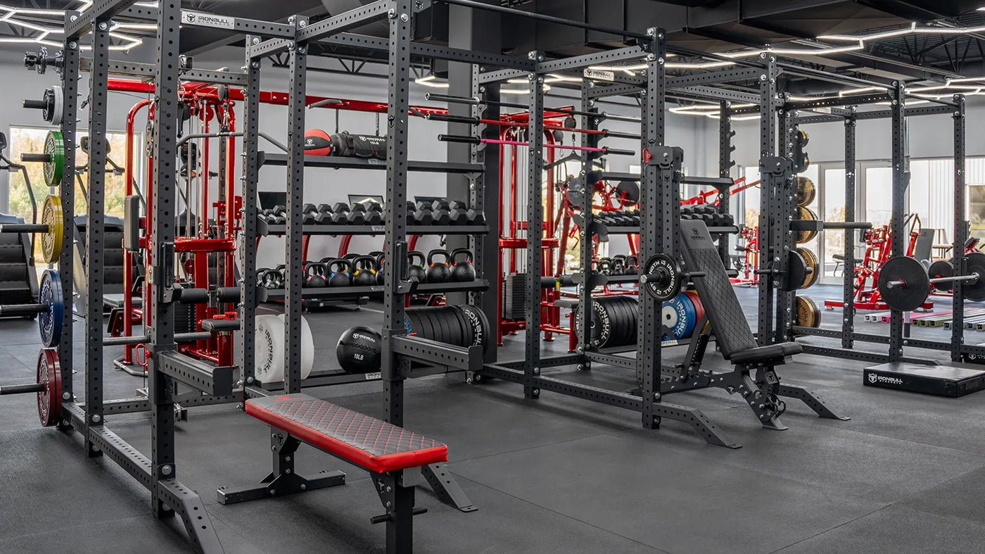 Gym interior with weightlifting equipment including racks, dumbbells, and benches.
