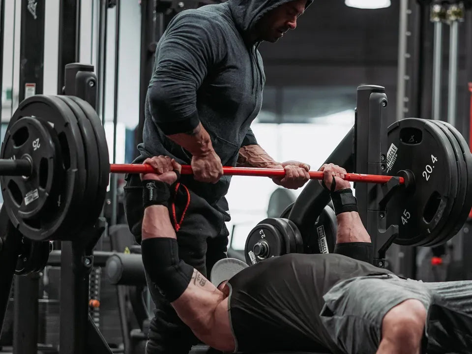 Person performing a bench press with a spotter in a gym setting