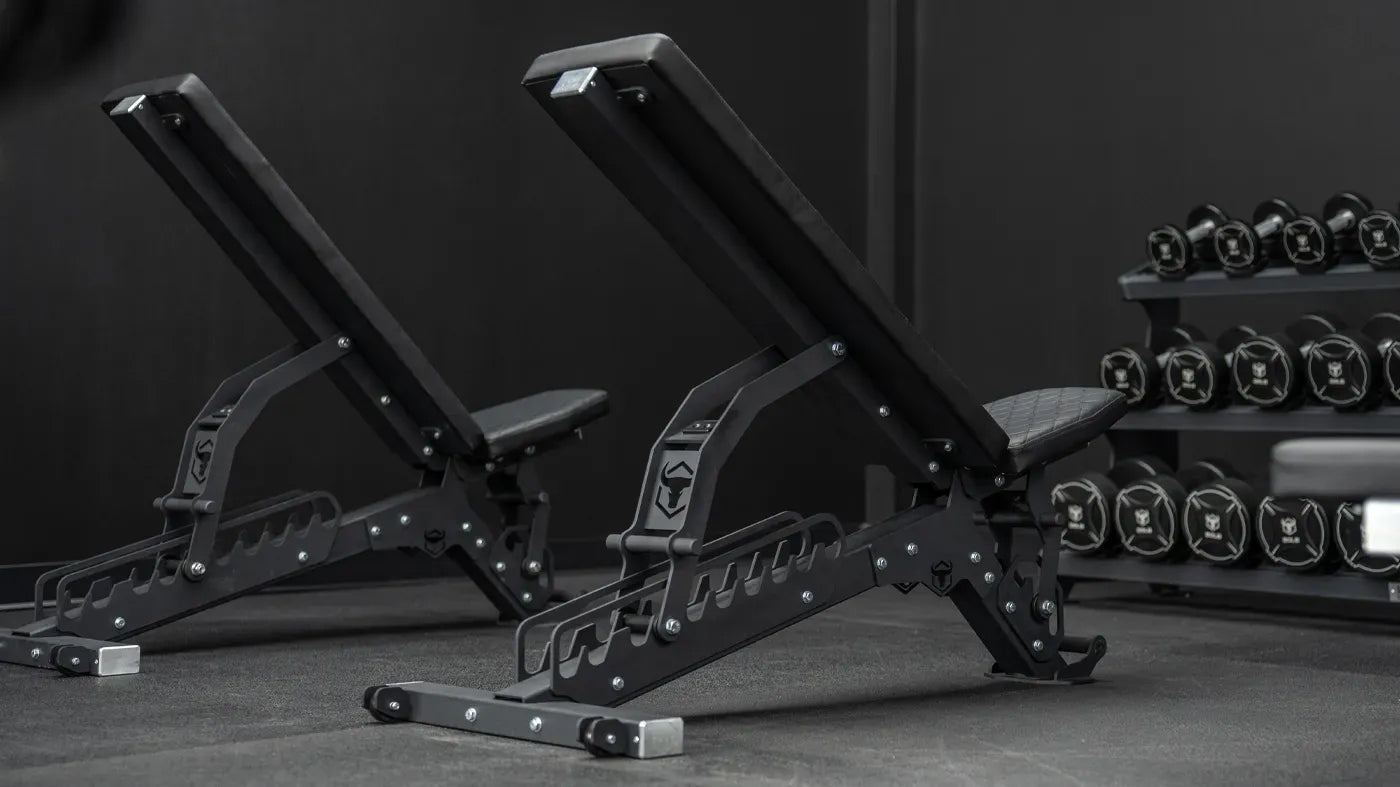 Pair of adjustable weight benches in a gym setting with weights in the background.
