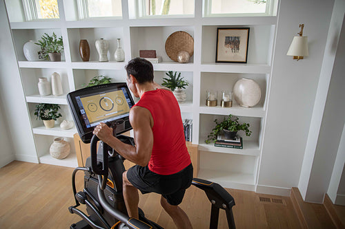 Person using a stationary bike in a home setting with a bookshelf in the background