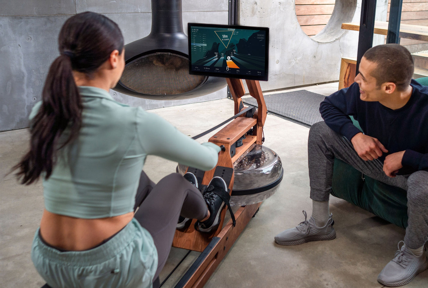 Two people using a home exercise machine with a screen displaying workout data.