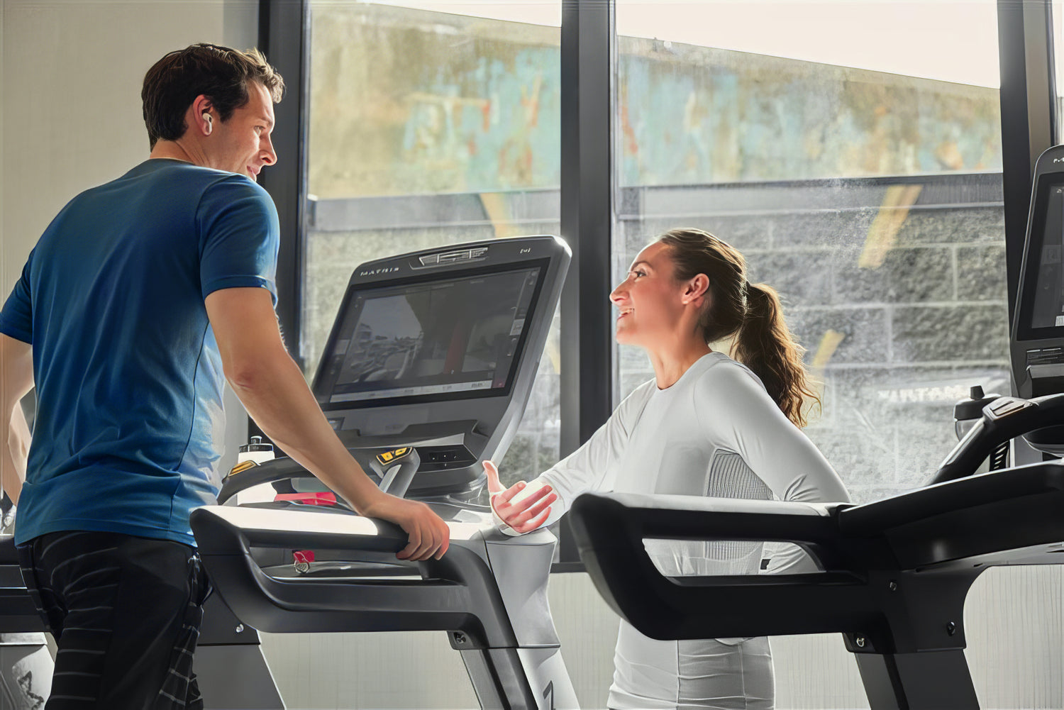 Two people on treadmills in a modern indoor setting with large windows.