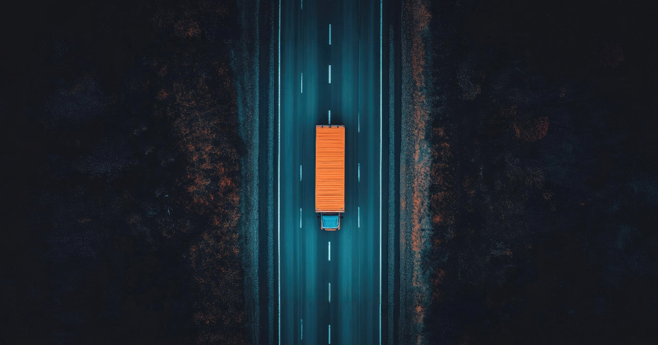 A truck with an orange trailer is driving on a dark road at night.