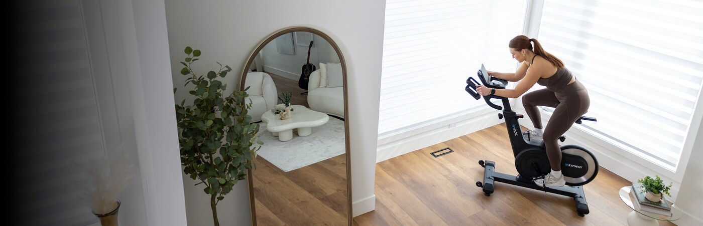 Woman exercising on a bike in a home setting with a mirror and plants.