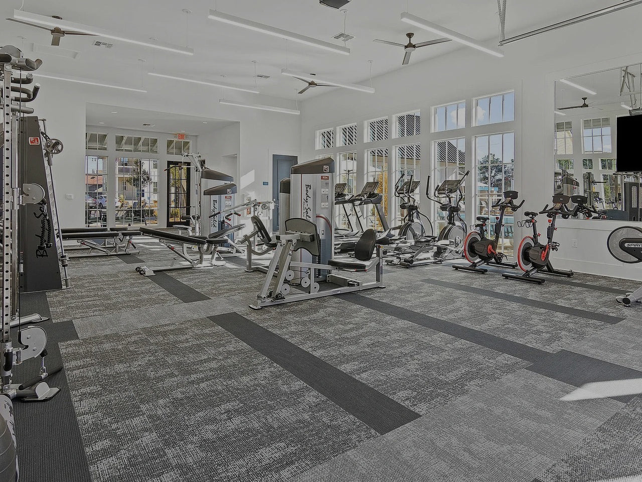 Gym interior with various exercise equipment and large windows.