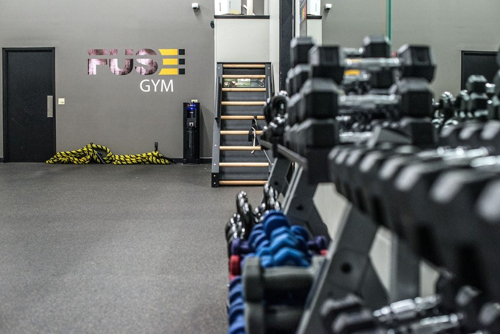 Gym interior with dumbbells and 'Fuse Gym' branding on the wall.