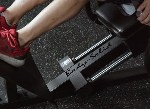 Person using a Body-Solid exercise machine with red shoes on a dark surface