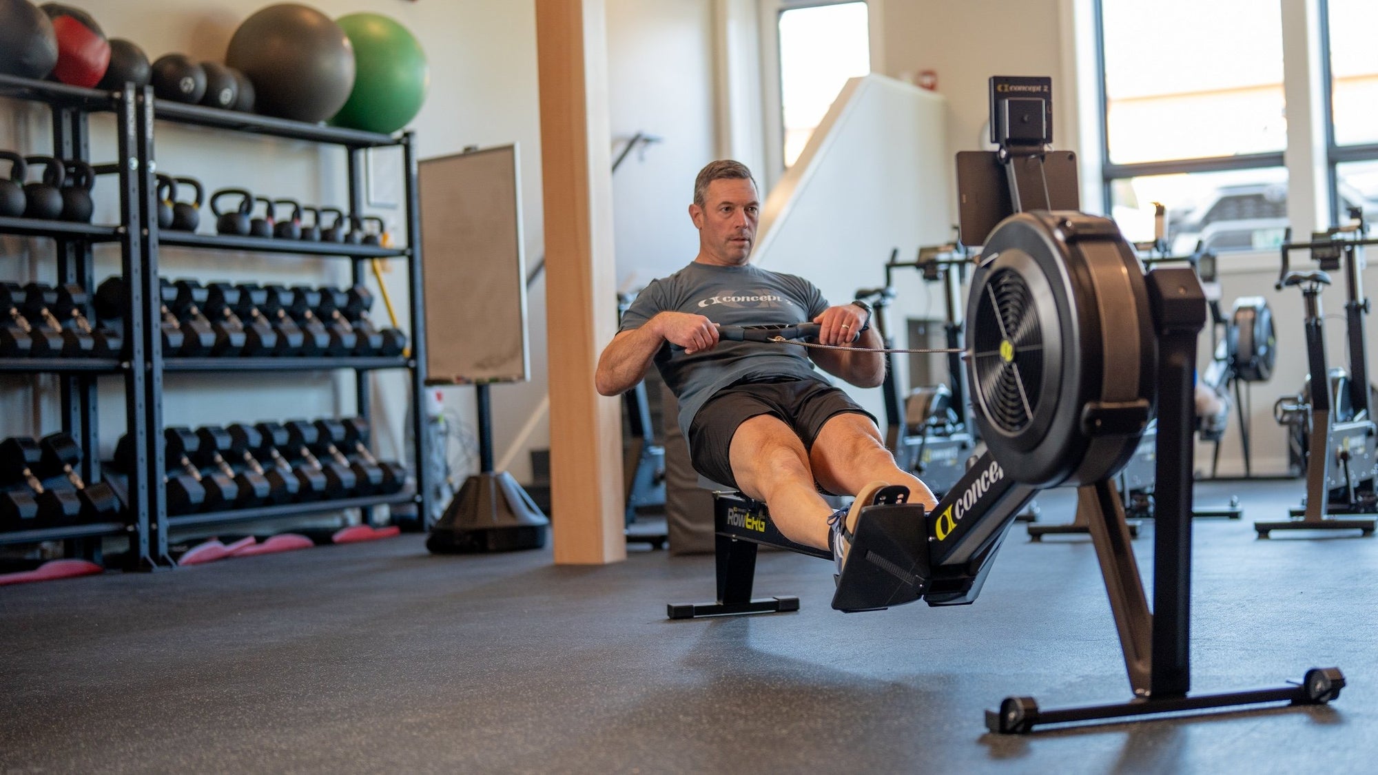 Man using a rowing machine in a gym setting with exercise equipment around.