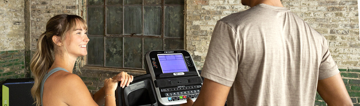 Woman using a Fitway 1500T treadmill with a man standing behind her, in a home setting.