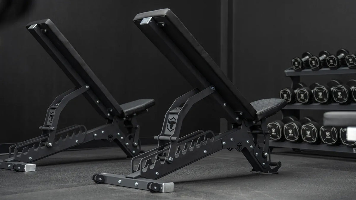 Pair of adjustable weight benches in a gym setting with weights in the background.