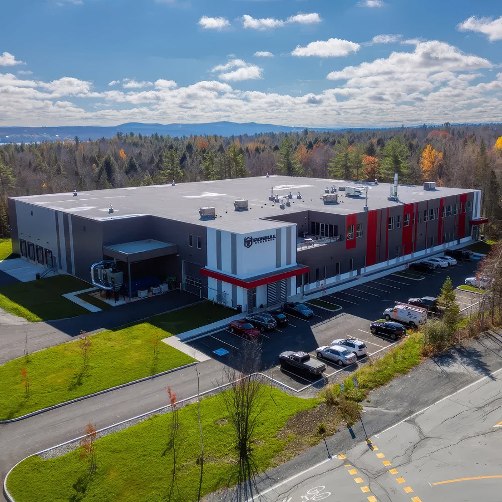 A large industrial building with a red and gray facade, surrounded by trees and a clear sky.
