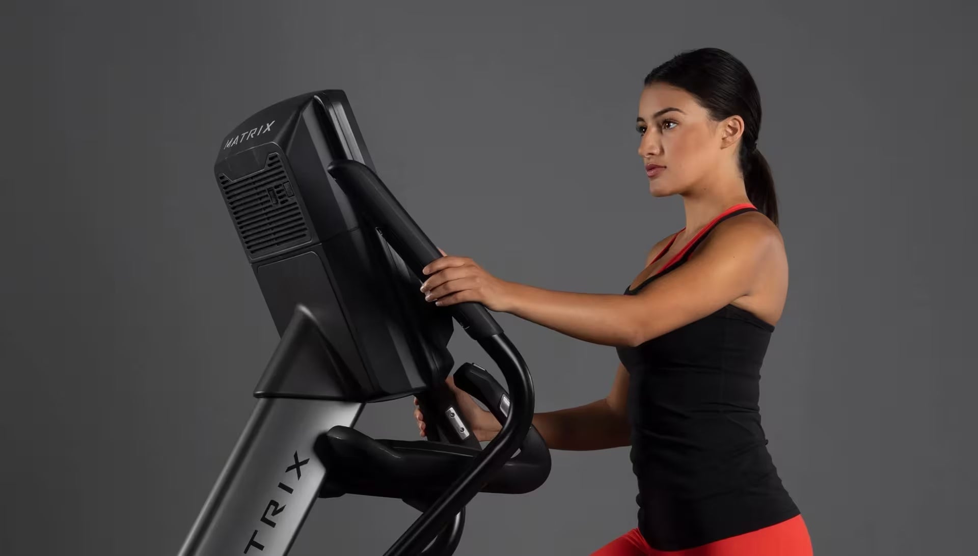 Woman exercising on a Precor elliptical machine against a gray background