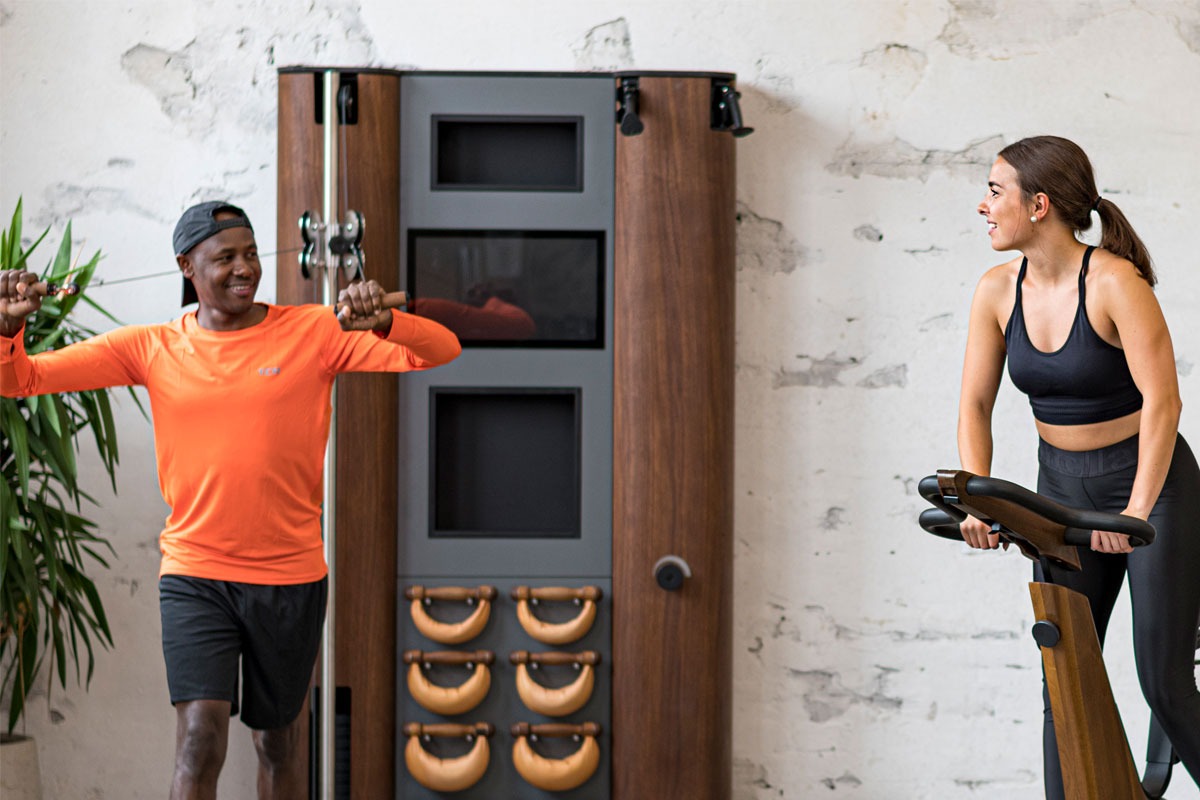 Two people exercising in a home gym setting with a wooden exercise machine.