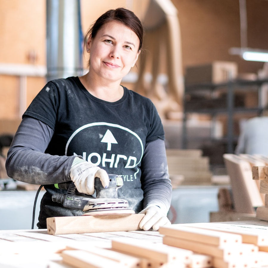 Woman working with wood in a workshop wearing a branded shirt.