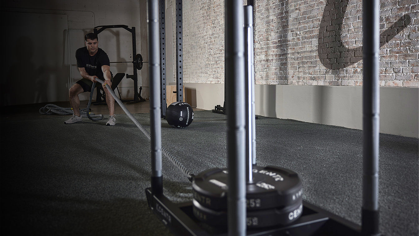 Person using resistance bands in a gym setting with weights and gym equipment visible.