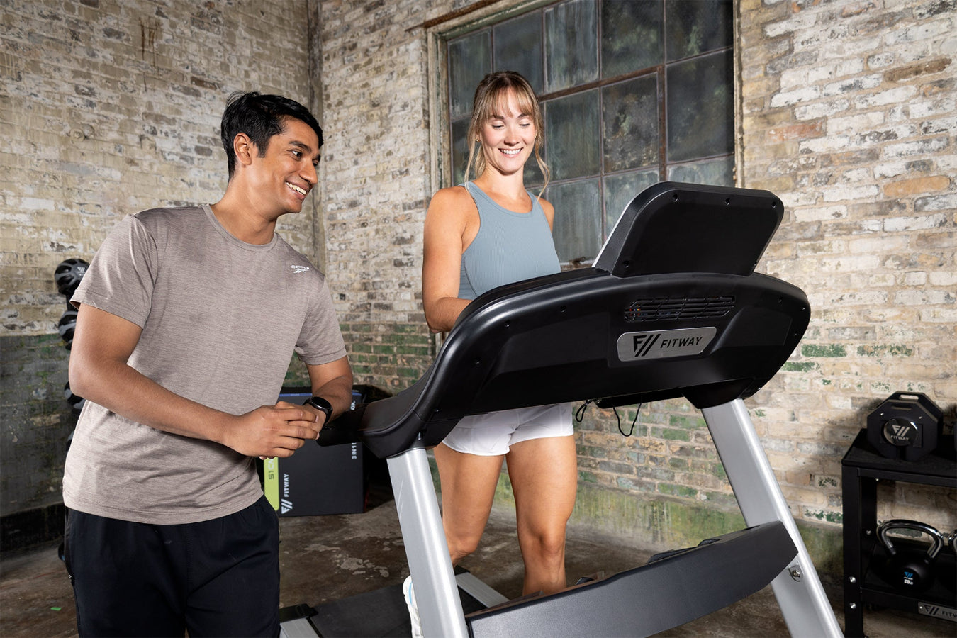 Two people using a treadmill in a rustic indoor setting
