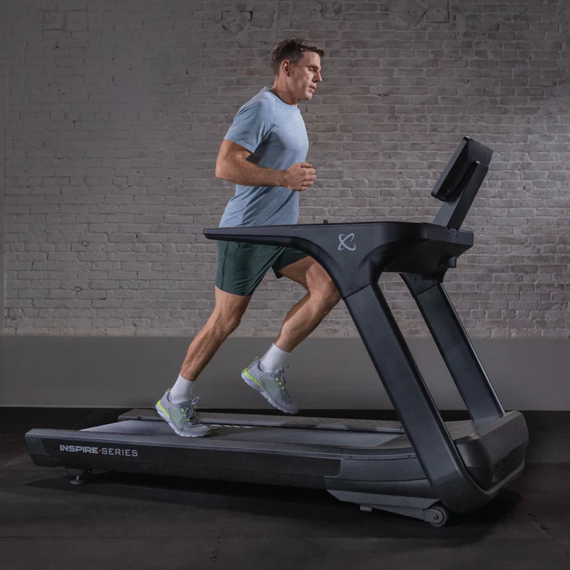 Man running on a treadmill in a gym setting with a brick wall background