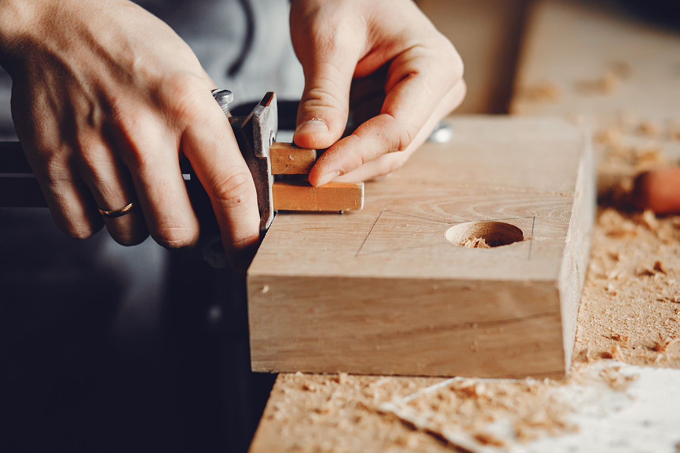 Person using a hand tool on a wooden block with visible wood shavings.