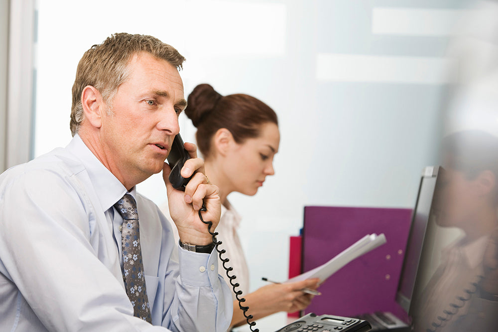 Man on phone with woman at desk in office setting