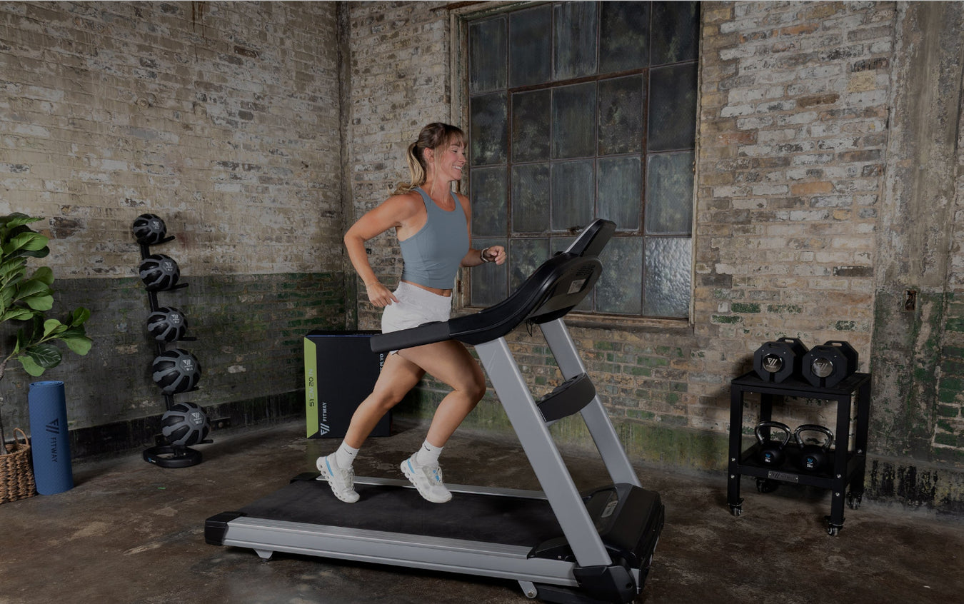 Woman running on a treadmill in a rustic indoor setting with exercise equipment around.