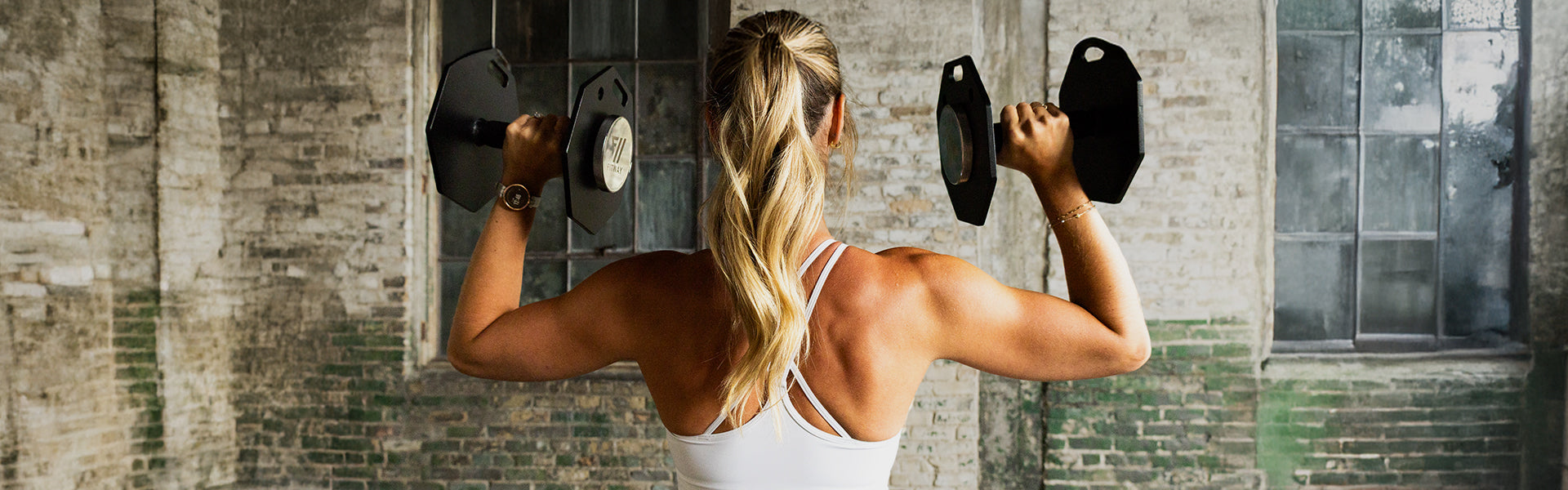 Woman lifting dumbbells against a brick wall