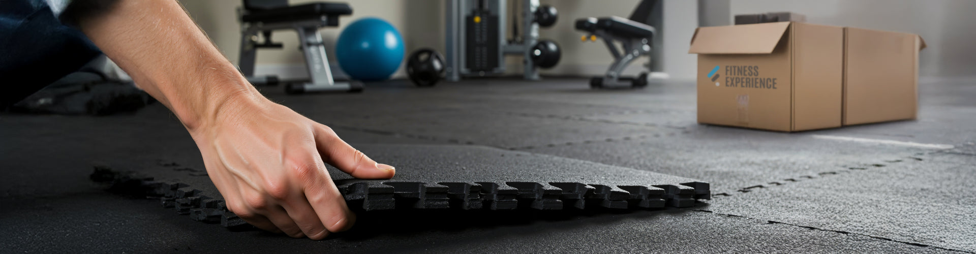 Person arranging black mats on a floor with gym equipment in the background